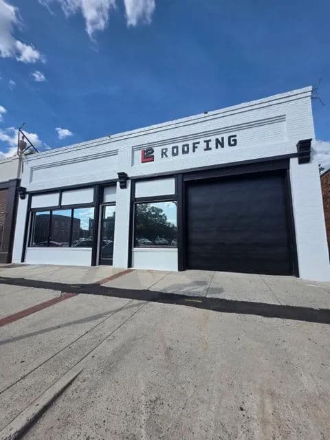 Modern roofing business storefront with large windows and prominent signage against a blue sky.