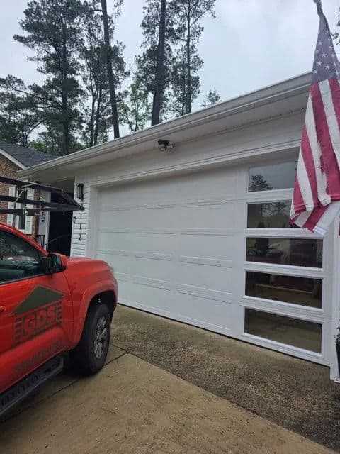 Red truck parked near a modern white garage with windows and an American flag.