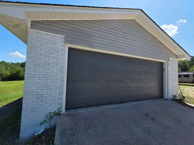 Gray garage door on a modern house with white brick exterior and clear blue sky.