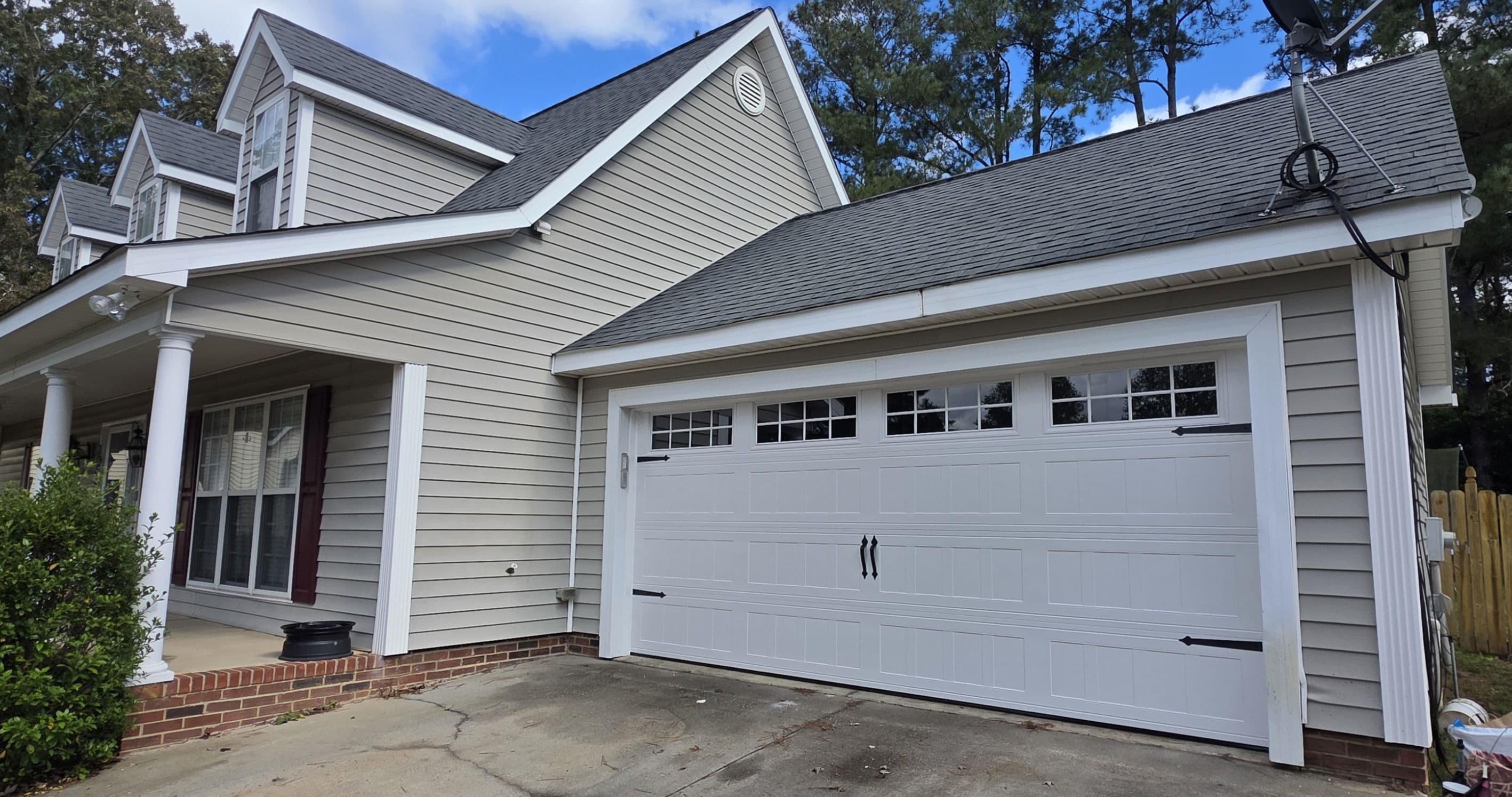 Modern white garage door on a suburban home with gray siding and a pitched roof.