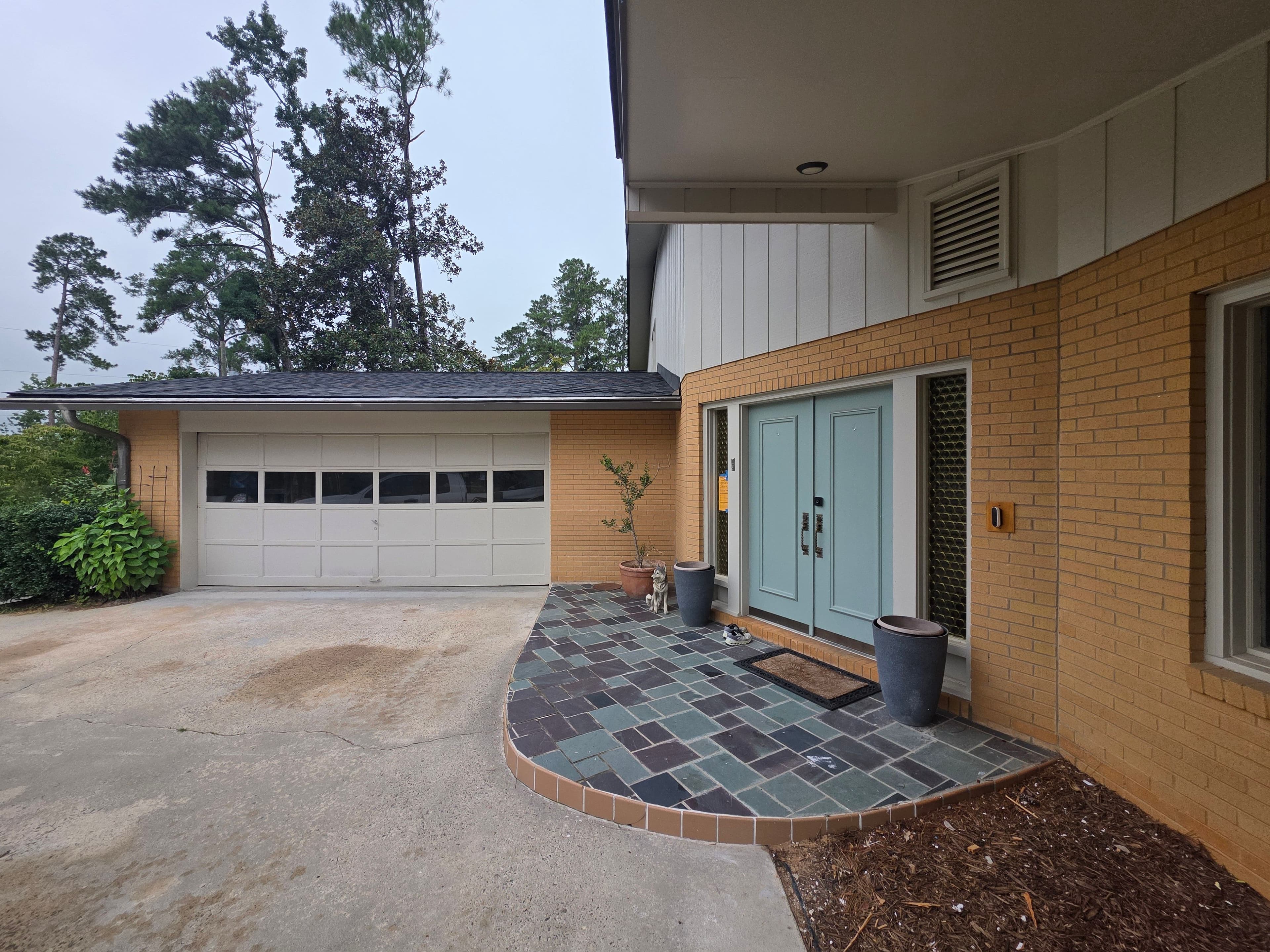 Modern home entrance with blue door, stone pathway, and garage, surrounded by greenery.