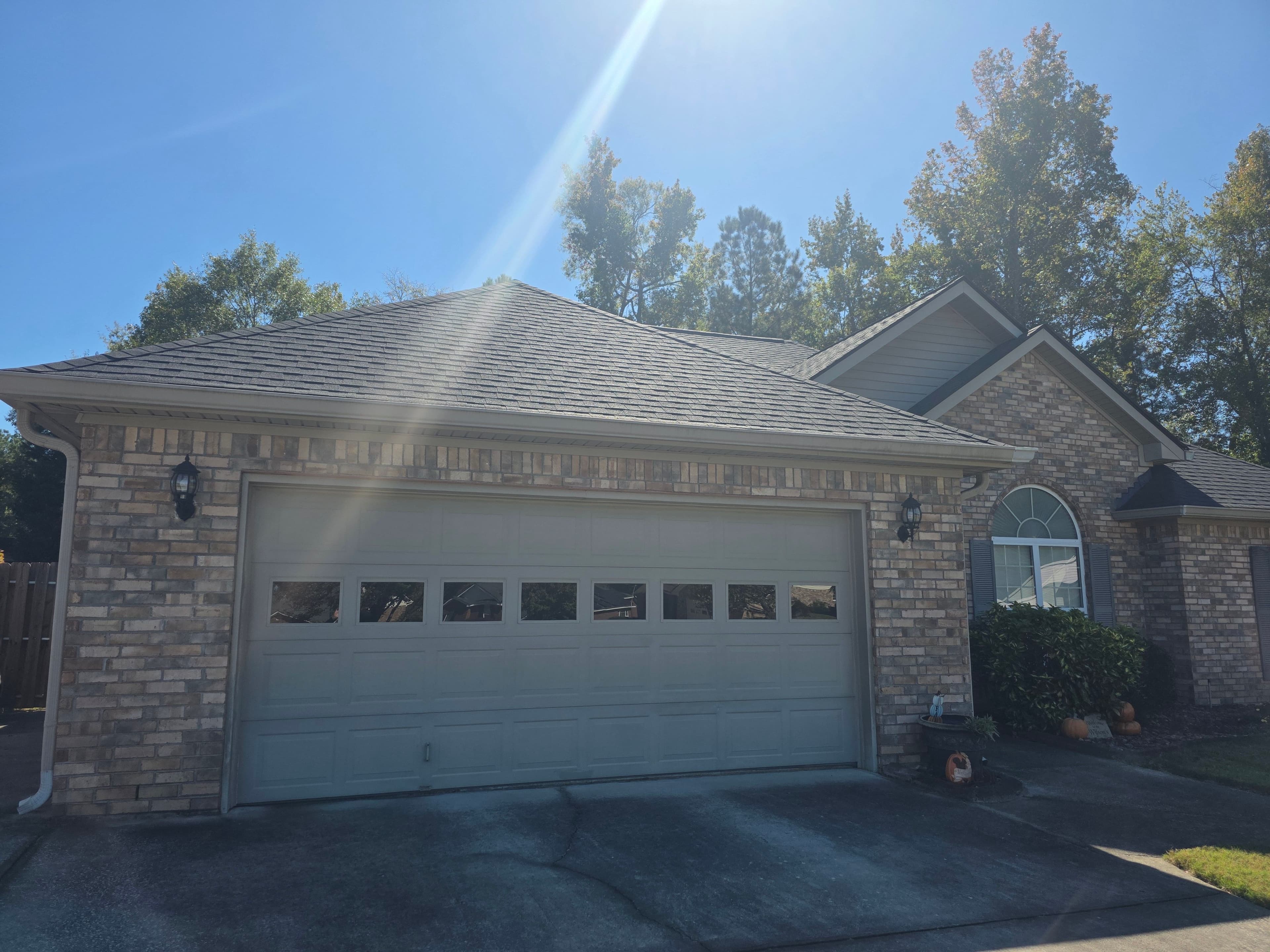 Brick house with a double garage, clear blue sky, and autumn trees in the background.