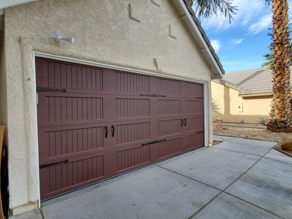 Modern brown garage door with decorative handles, leading to a landscaped driveway.