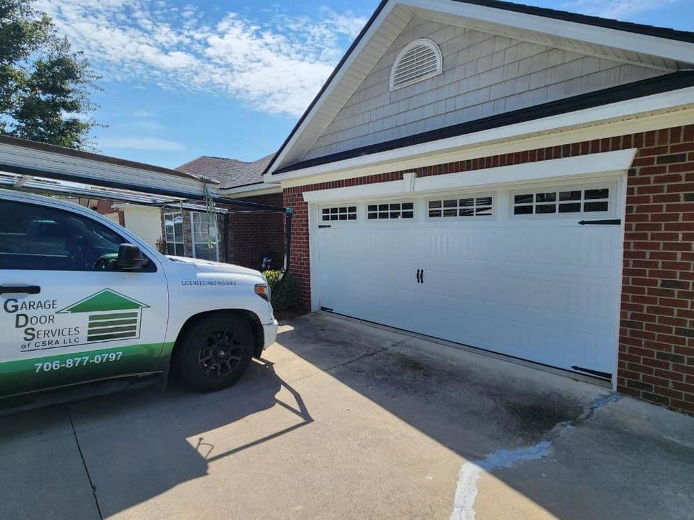 Garage door services vehicle parked by a residential garage with a closed white garage door.