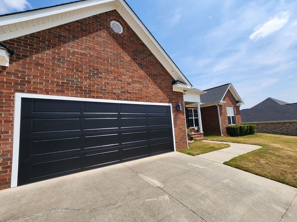 Modern brick house with a black garage door and well-maintained landscaping on a sunny day.