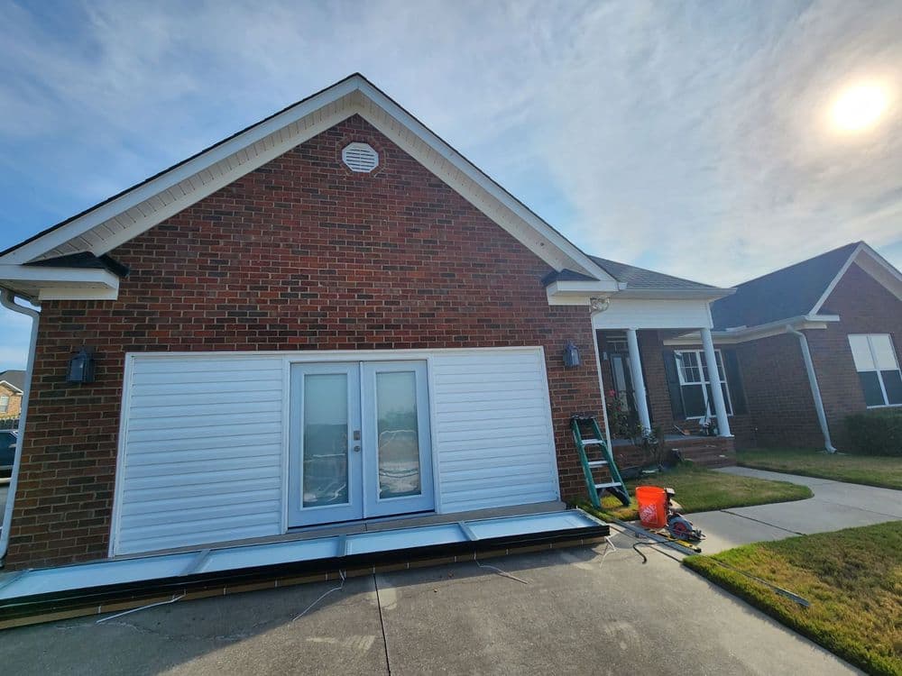 Brick home exterior with new white siding installation and a sunny sky in the background.