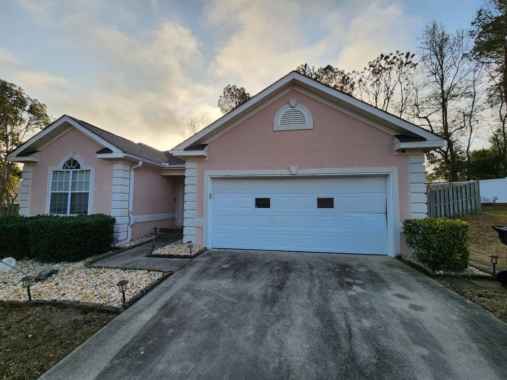 Front view of a pink single-family home with a garage and landscaped yard.