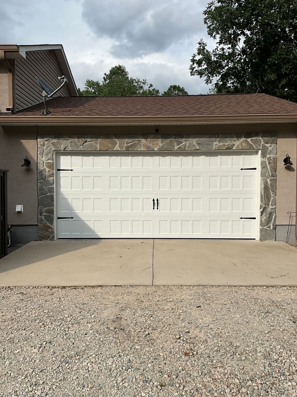 White garage door with stone accent, situated on a gravel driveway in residential area.