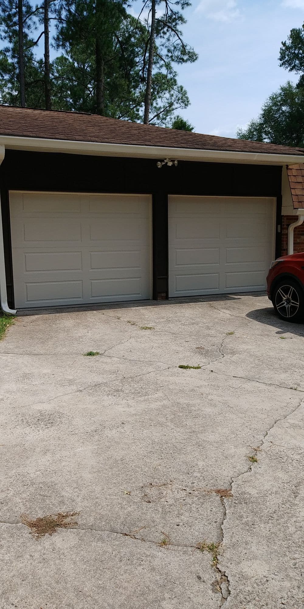 Two white garage doors on a concrete driveway under a clear blue sky. Green trees in background.