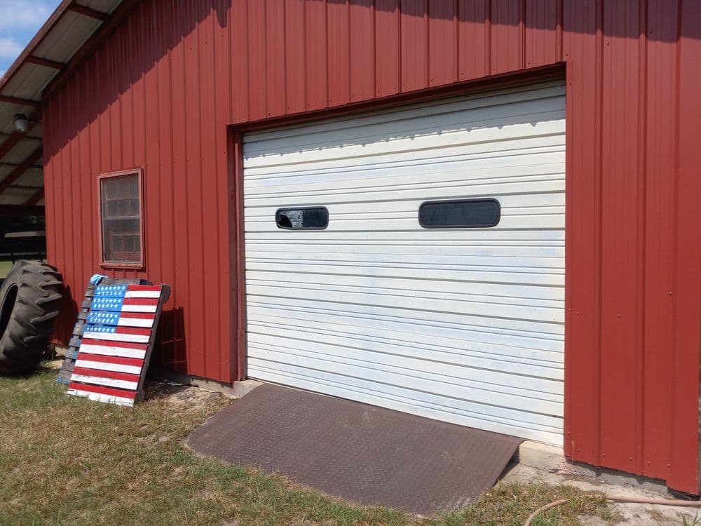Red barn exterior with a white garage door and an American flag painting nearby.