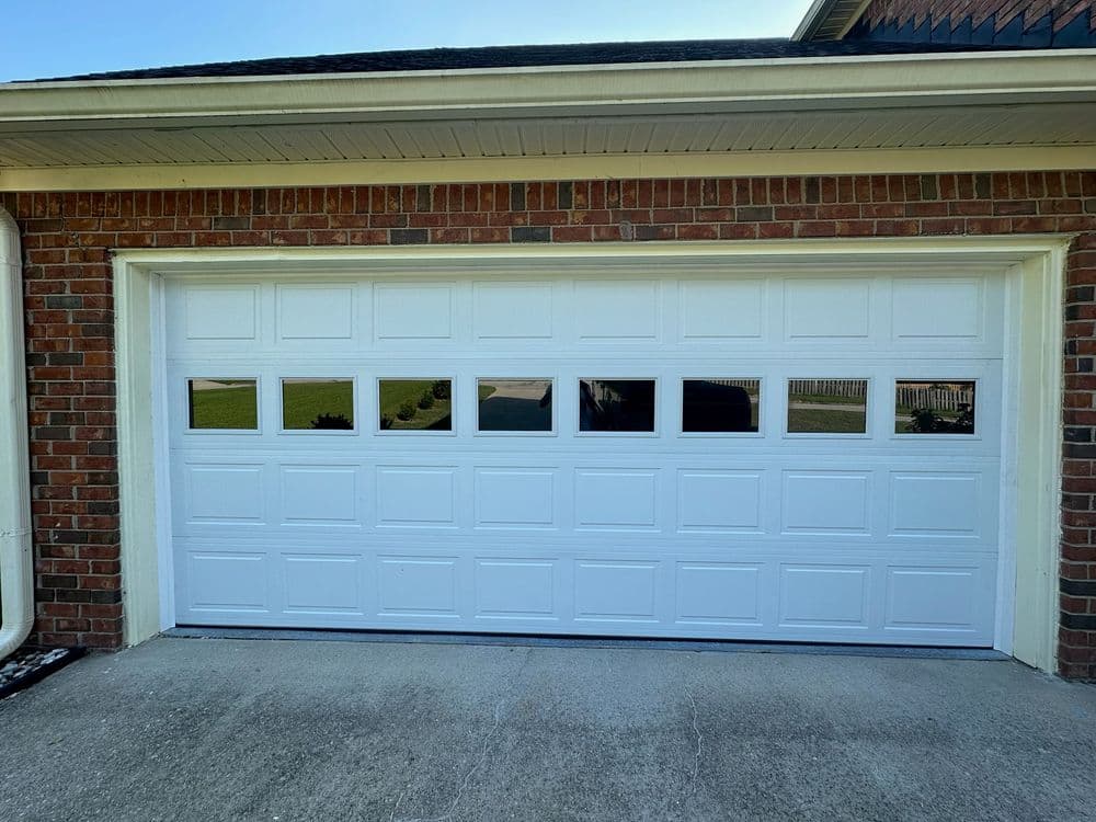 White garage door with windows, set against a brick wall and clear sky. Modern design.