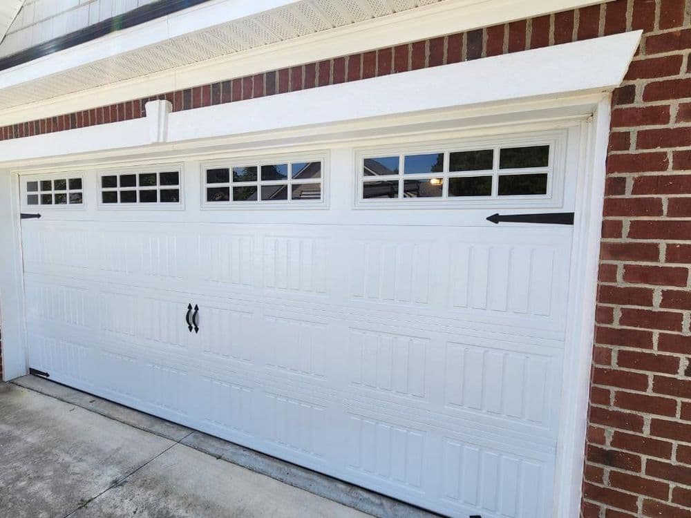 White garage door with decorative windows, installed on a brick exterior home.