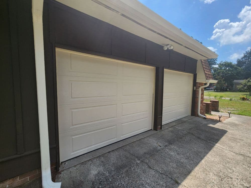 Two white garage doors on a residential home with a concrete driveway and blue sky background.