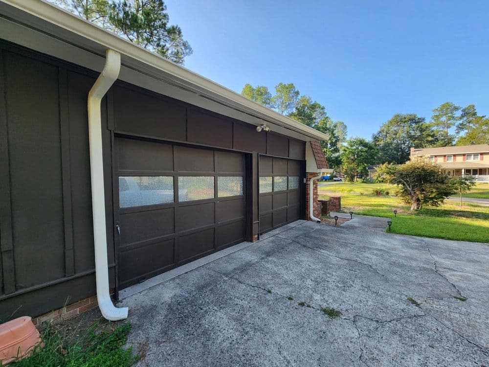 Modern garage with two doors and a concrete driveway, surrounded by greenery.