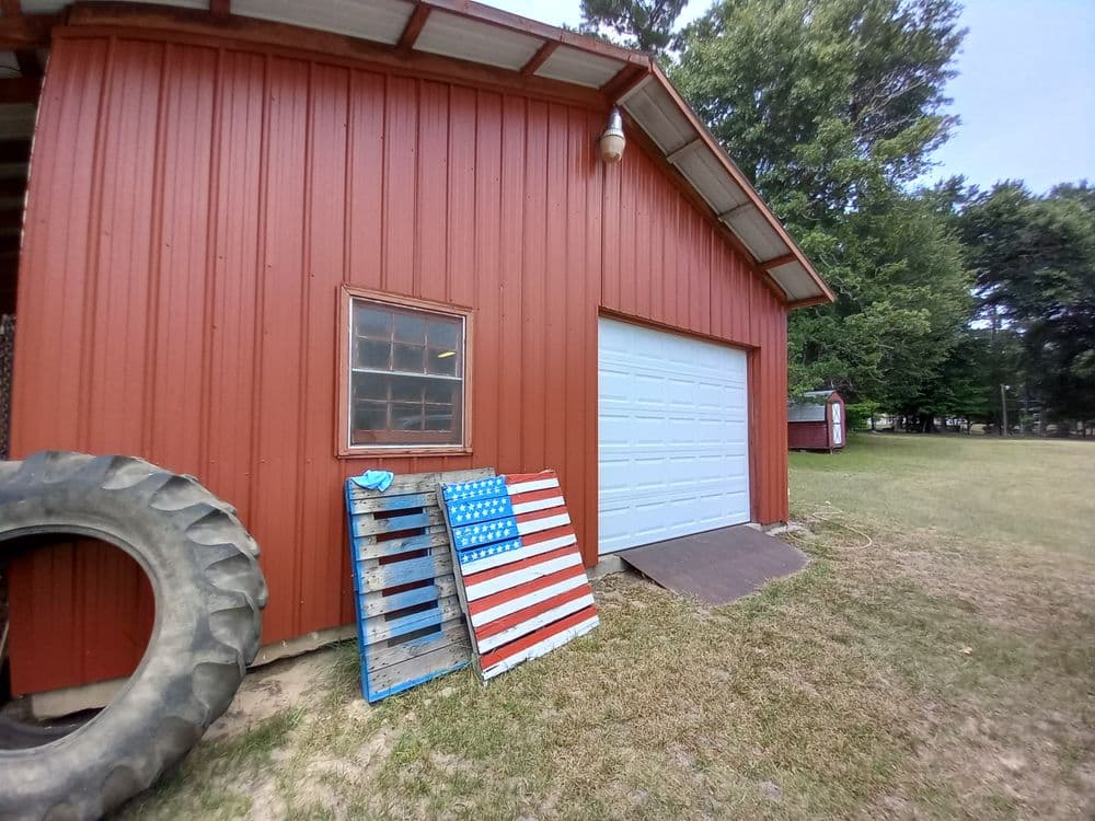 Red barn exterior with a white garage door, wooden pallets painted like the American flag, and tire.