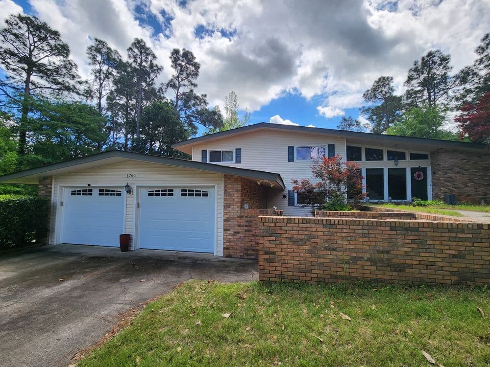 Modern two-story brick home with large windows, lush landscaping, and a two-car garage.