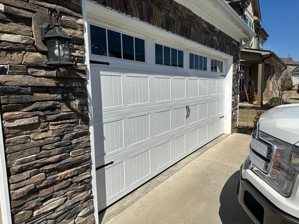 White garage door with decorative hardware next to stone exterior and parked vehicle.