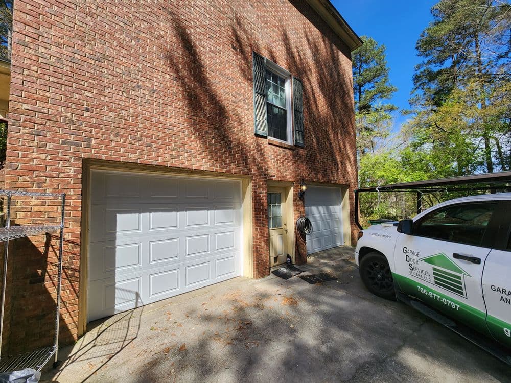Residential garage with two white doors and a service vehicle parked in front.