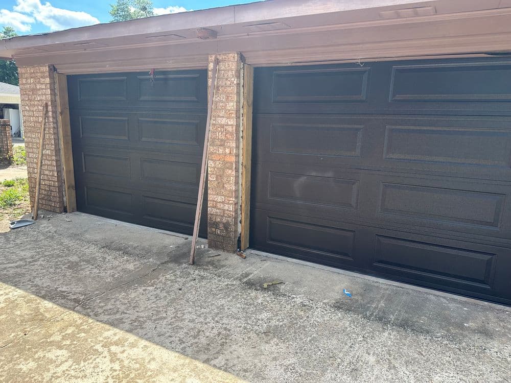 Newly installed black garage doors with a concrete driveway and brick facade.
