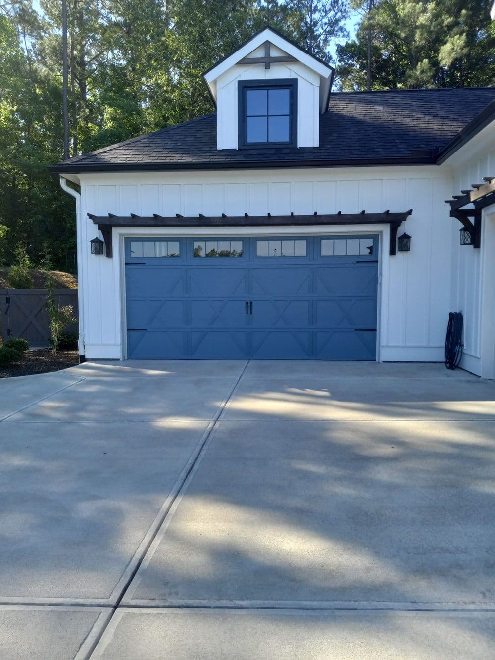 Blue garage door with windows, modern home exterior, surrounded by greenery and concrete driveway.