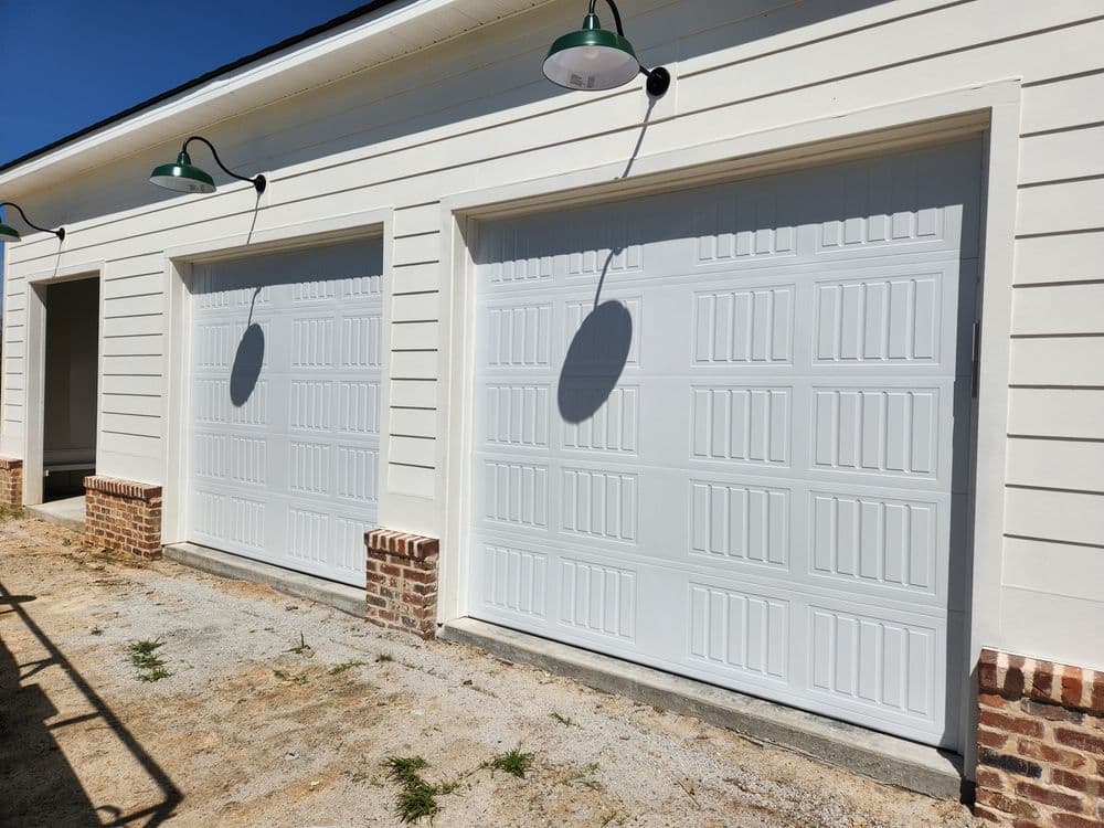 White garage doors on a beige house exterior with green light fixtures and gravel driveway.