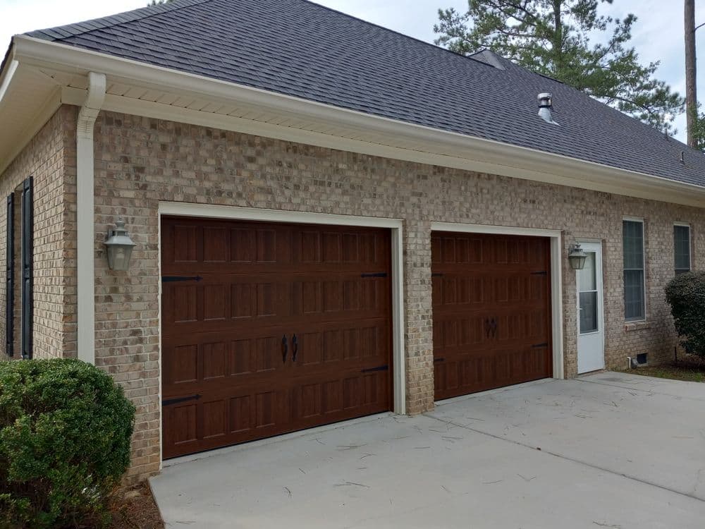 Brick house featuring two brown wooden garage doors and a side entrance.