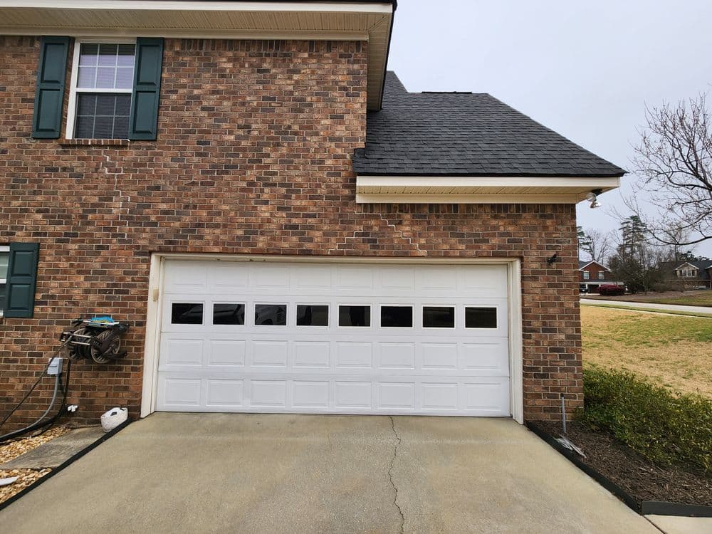 White garage door on a brick house with green shutters and a driveway.