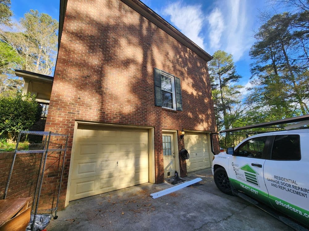 Two garage doors on a brick house with a service van parked nearby on a sunny day.