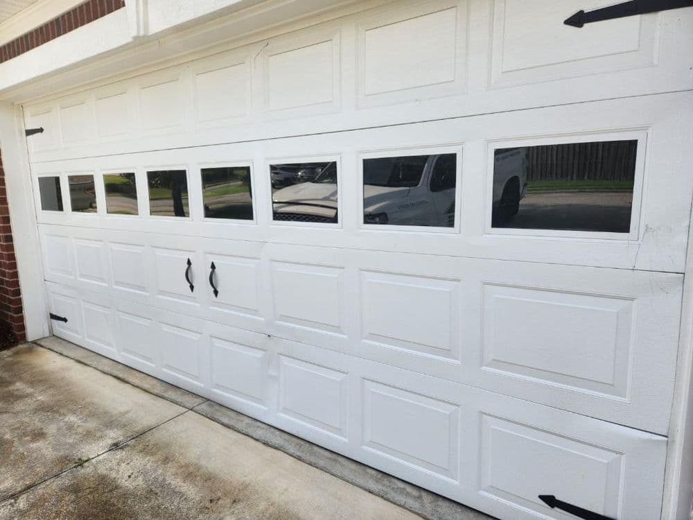 White overhead garage door with windows, black handles, and decorative hinges.