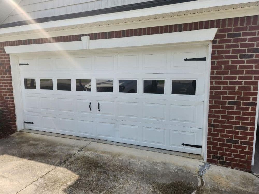 White garage door with windows and decorative handles on a brick wall.