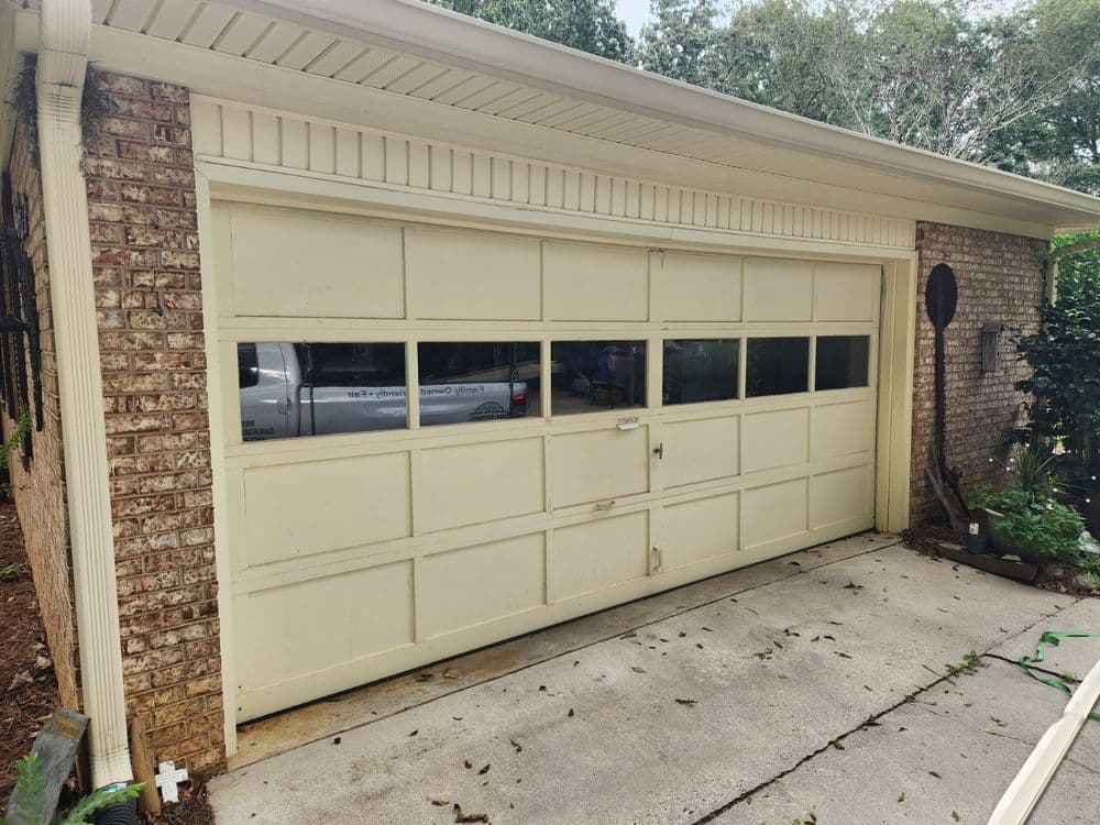 Yellow garage door with windows, surrounded by greenery and concrete driveway.