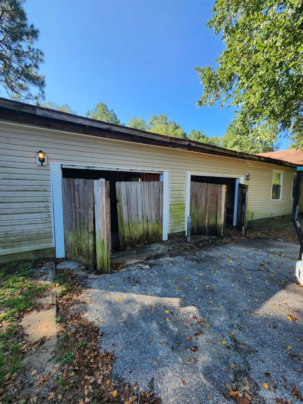 Abandoned building with weathered wooden garage doors and overgrown foliage.