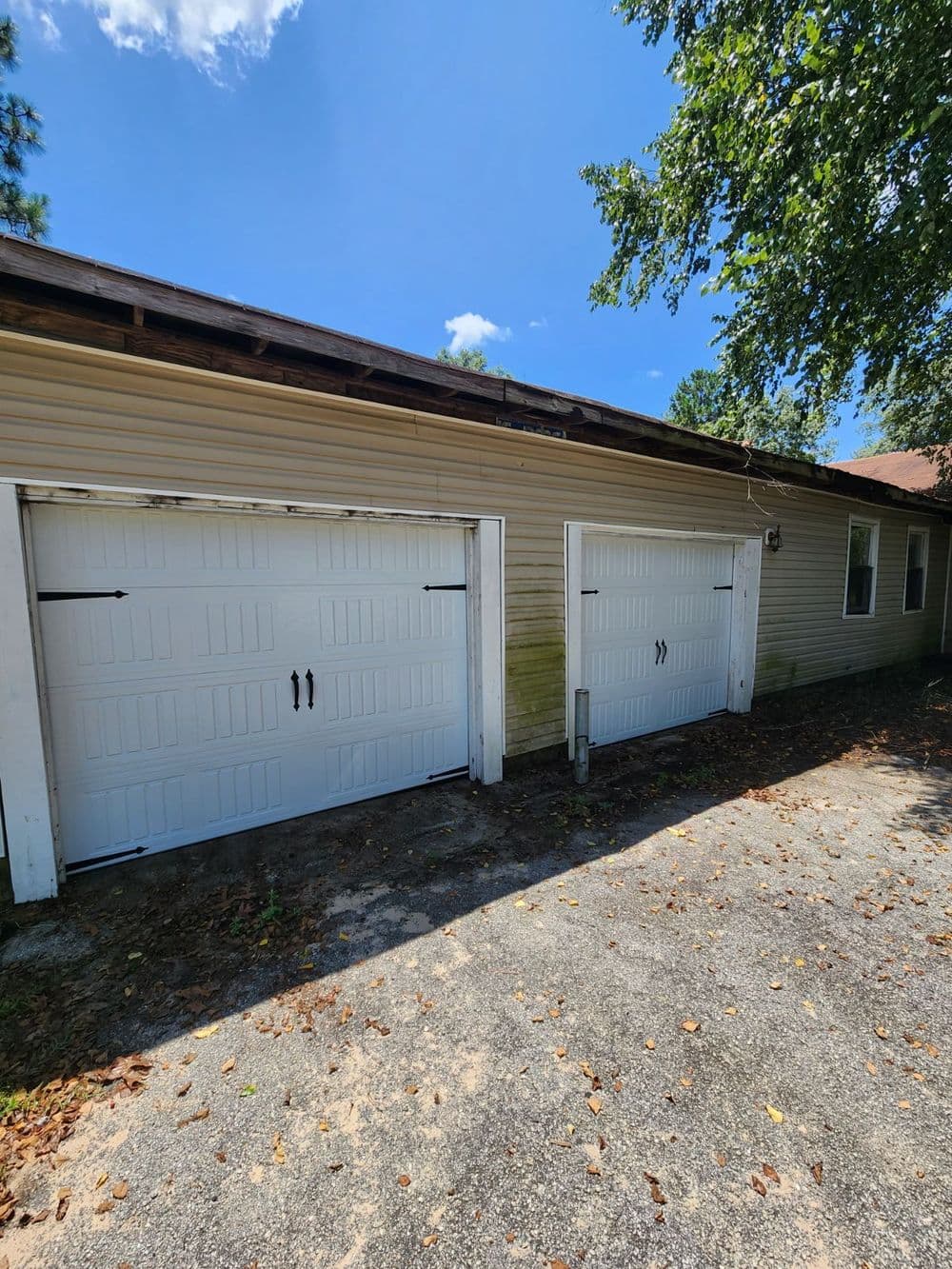 Two white garage doors on a residential home, surrounded by greenery and blue sky.