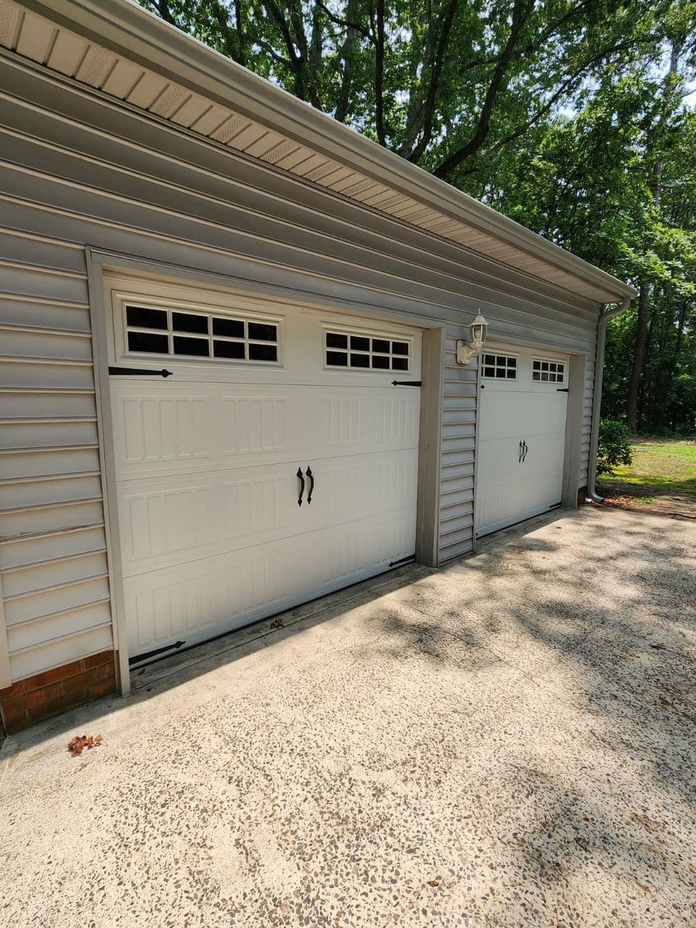Two white garage doors with decorative windows, set against a green outdoor backdrop.